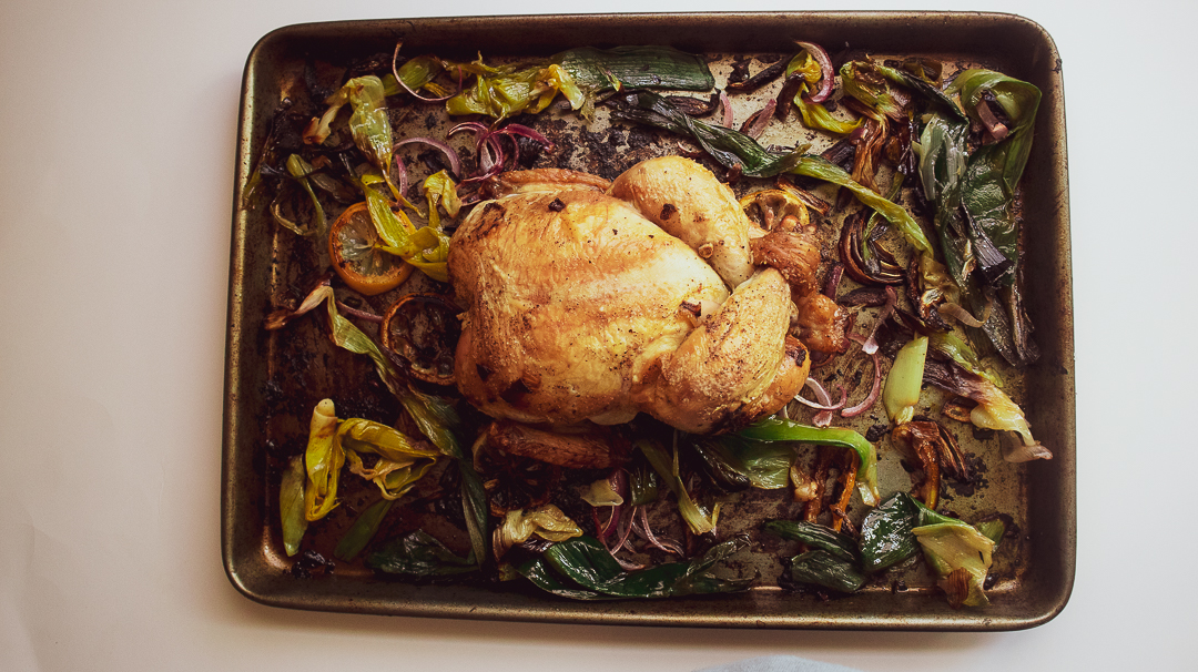 a whole chicken on a sheet pan with leek and roasted lemon