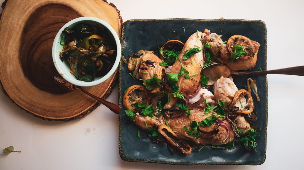 chicken with parsley garnish on a blue plate with a small bowl next to it with a green mixture inside.